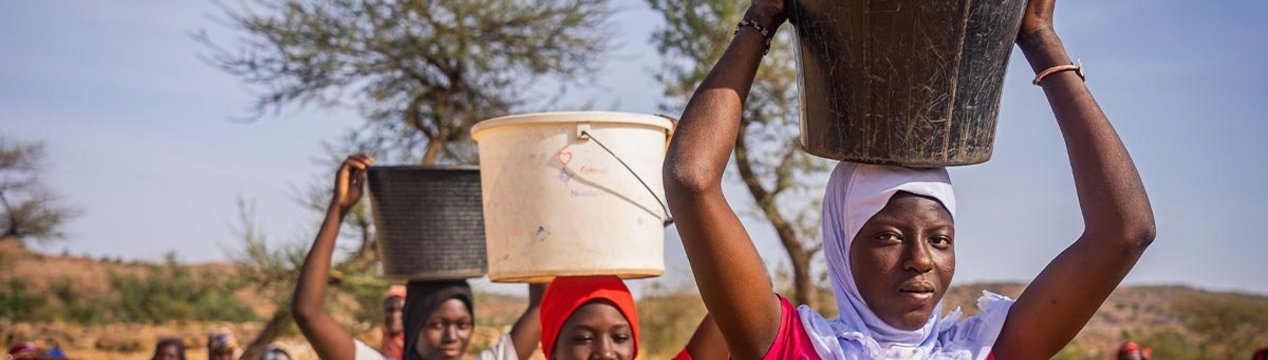 Drei malische junge Frauen tragen Wasser-Eimer auf dem Kopf