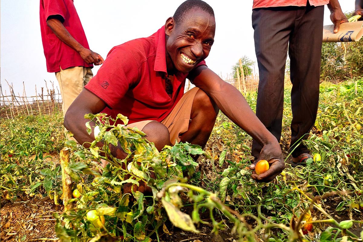 Ein Mann lacht in die Kamera während er die Ernte auf seinem Feld zeigt