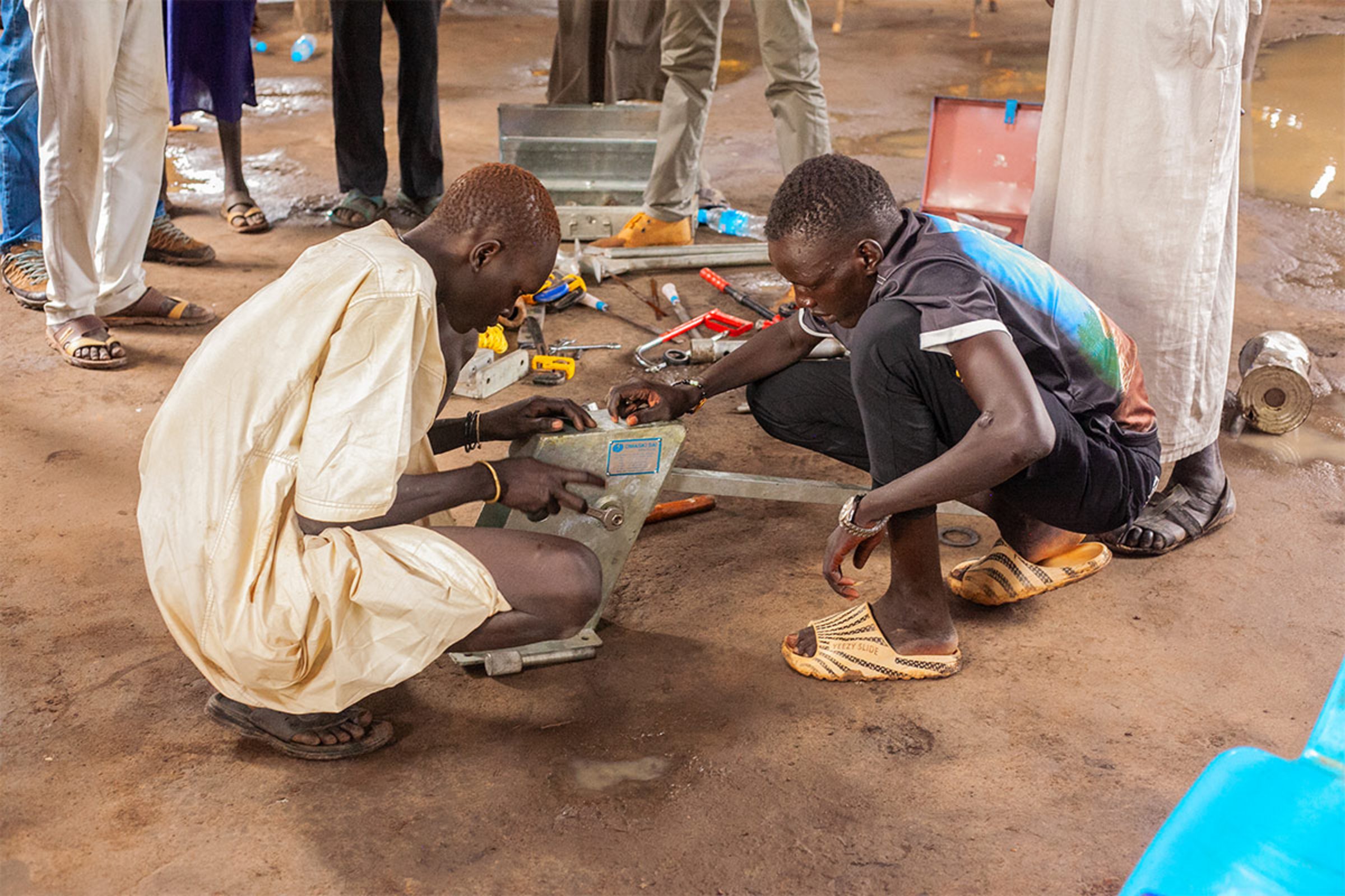 Zwei Männer lernen, wie sie eine Handpumpe reparieren