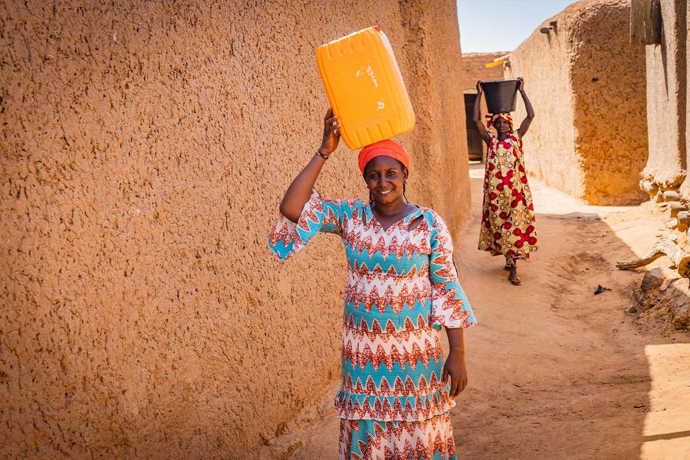 Zwei malische Frauen tragen Wasserkanister auf ihren Köpfen
