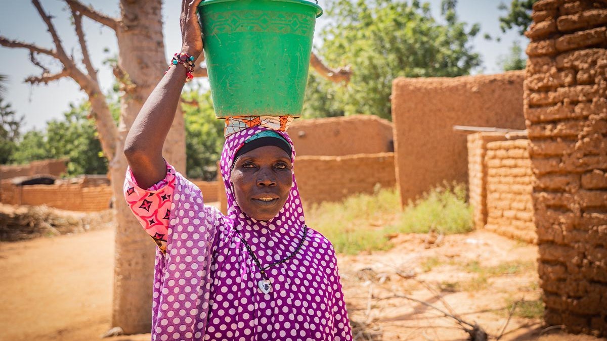 Eine malische Frau trägt einen grünen Eimer Wasser auf dem Kopf