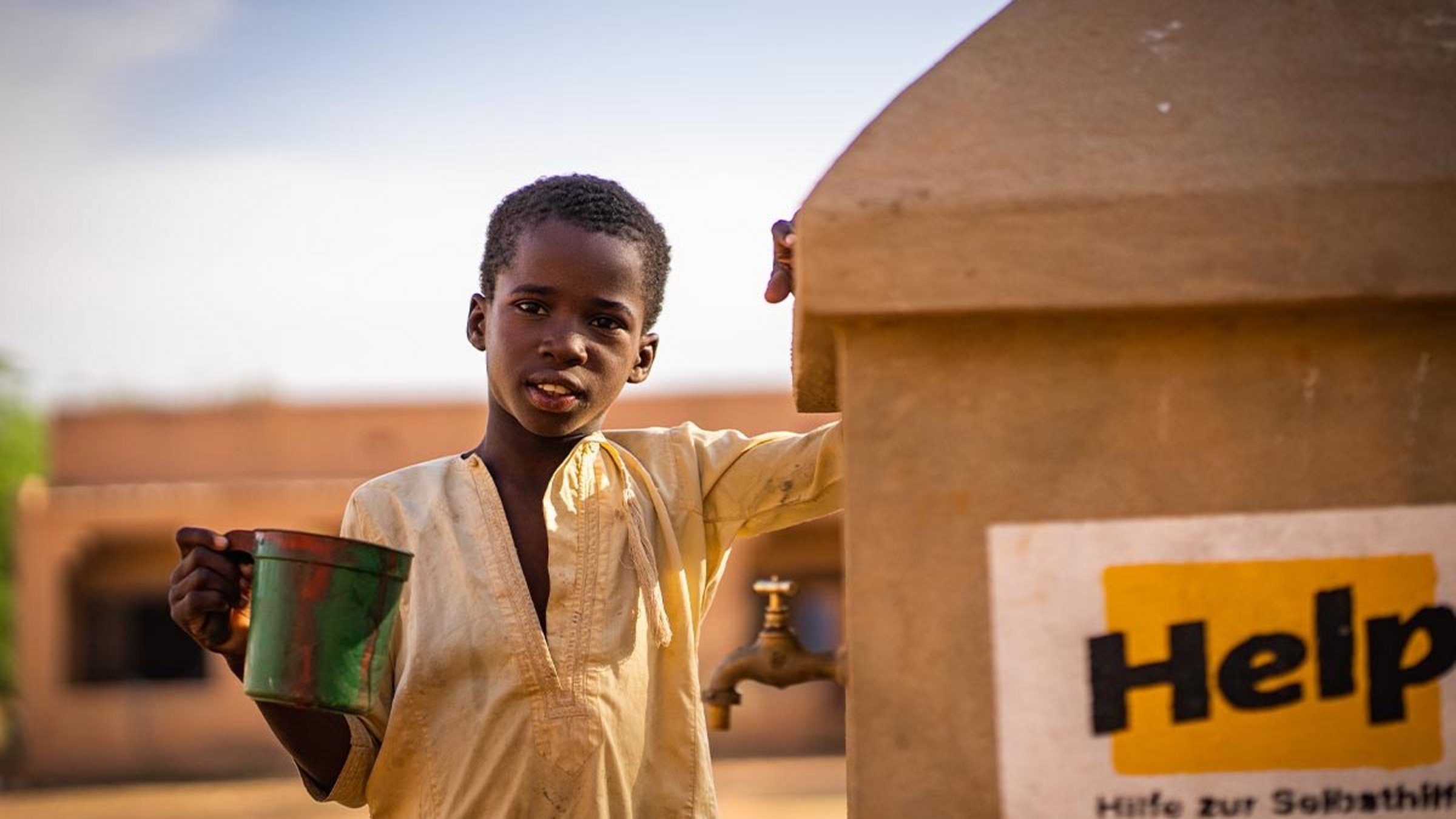 Ein Junge steht neben einem Help-Brunnen in Mali