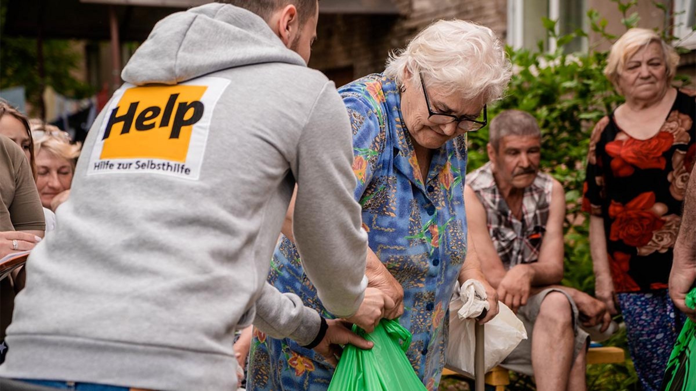 Ein Help-Mitarbeiter überreicht einer älteren Dame Hilfsgüter