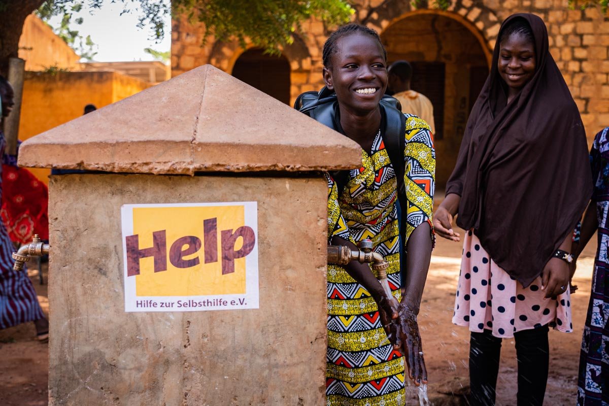 Ein malisches Mädchen wäscht sich die Hände an einem Brunnen von Help