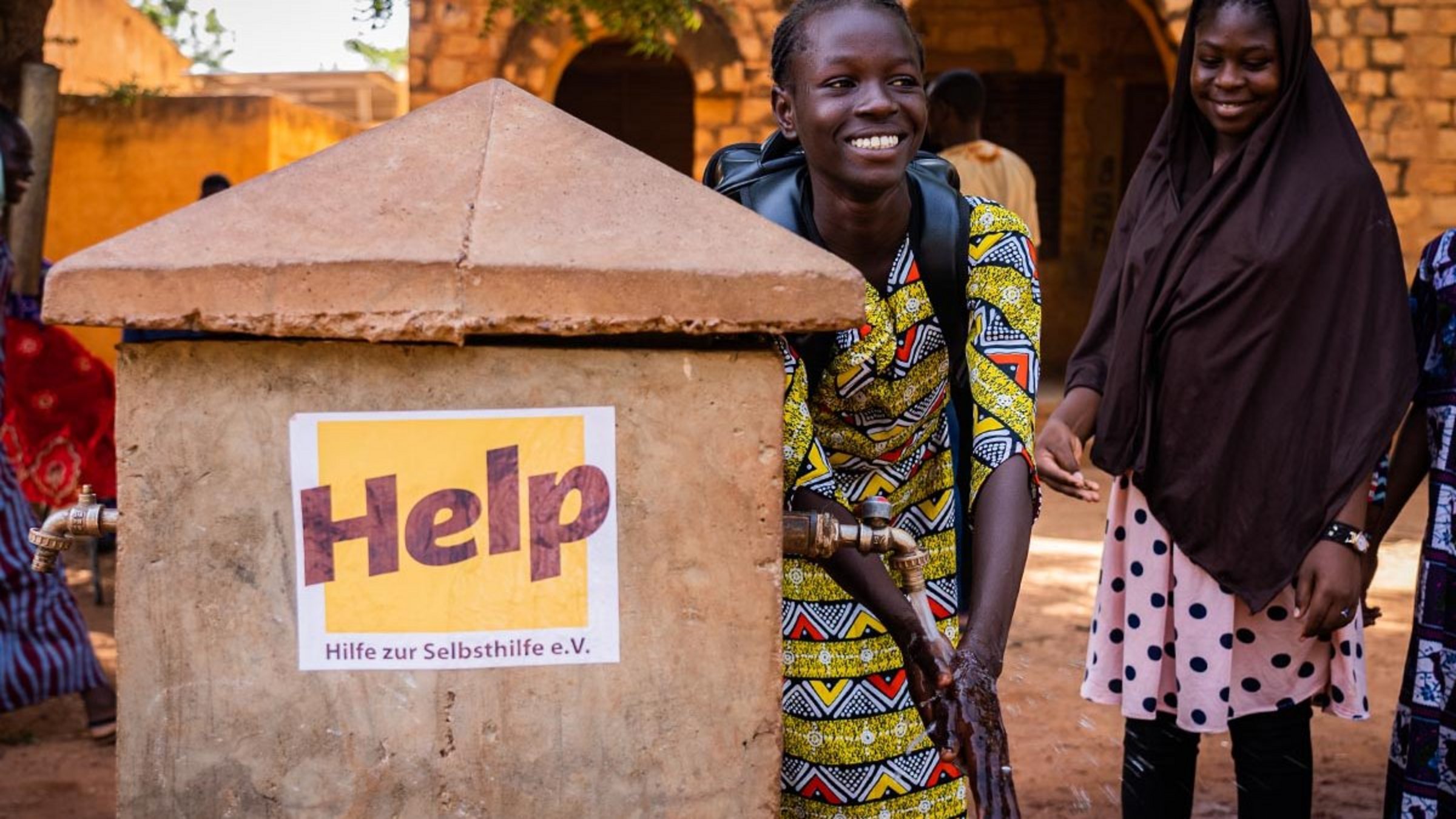 Ein malisches Mädchen wäscht sich die Hände an einem Brunnen von Help