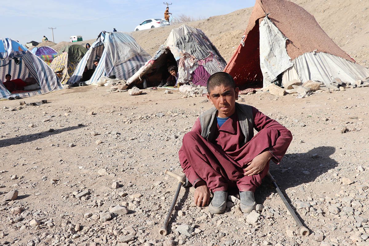 Ein afghanischer Jugendlicher mit Gehhilfen sitzt vor seinem Zelt