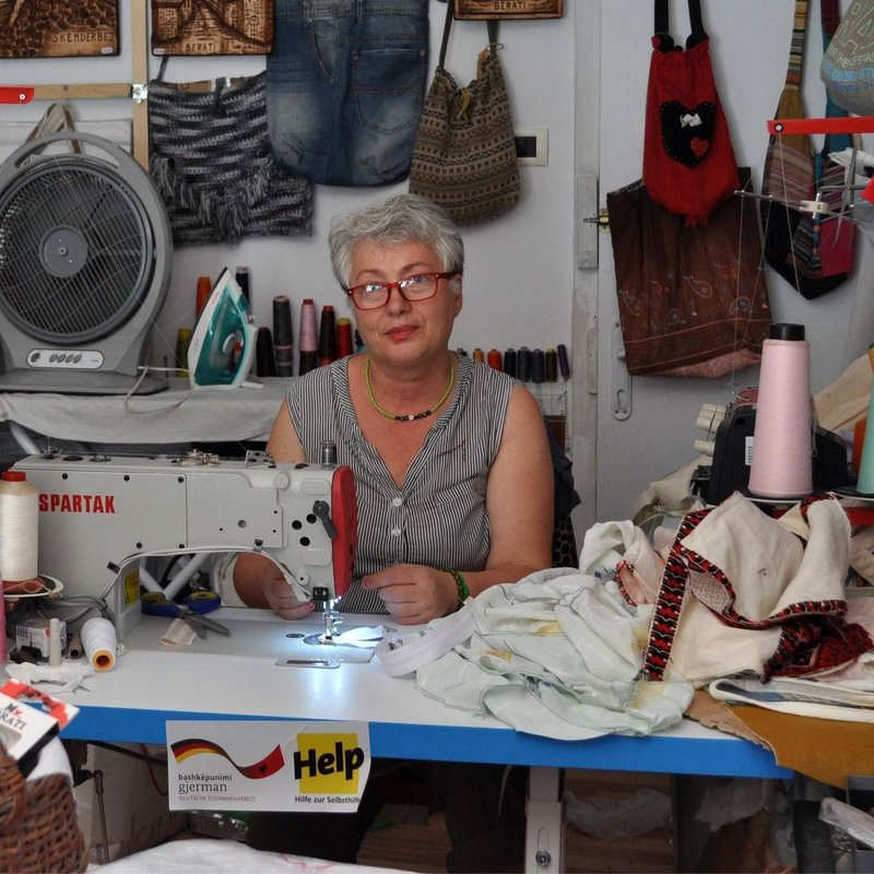 Eine Näherin in Albanien sitzt an ihrer Nähmaschine, die sie dank der Förderung von Help anschaffen konnte.