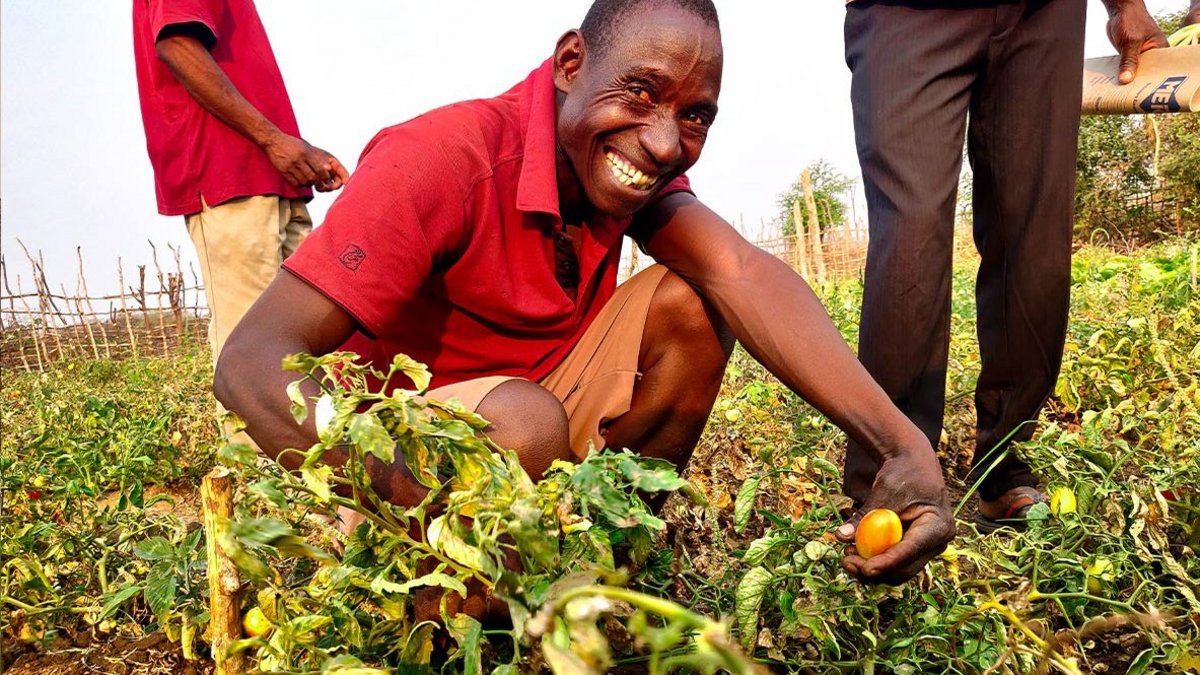 Ein Mann lacht in die Kamera während er die Ernte auf seinem Feld zeigt