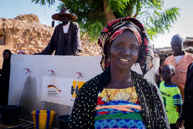 Eine Frau steht lachend vor einem Help-Brunnen