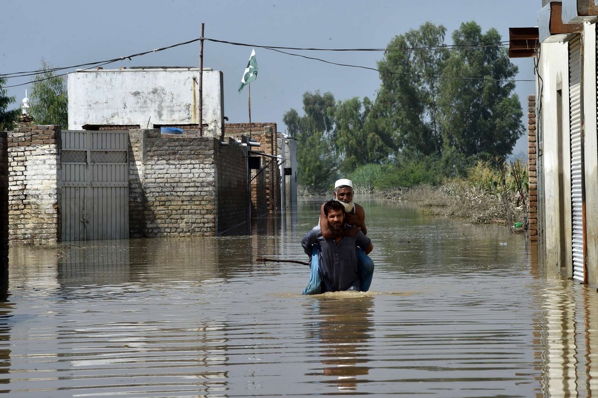 Zwei Männer waten durch Hochwasser in Pakistan