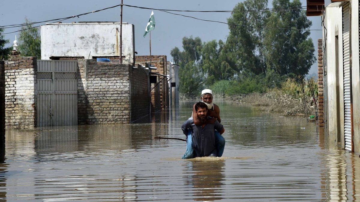 Zwei Männer waten durch Hochwasser in Pakistan