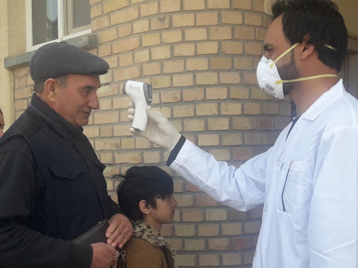 Help misst bei einem Mann in Afghanistan Fieber, um festzustellen, ob er Corona hat.