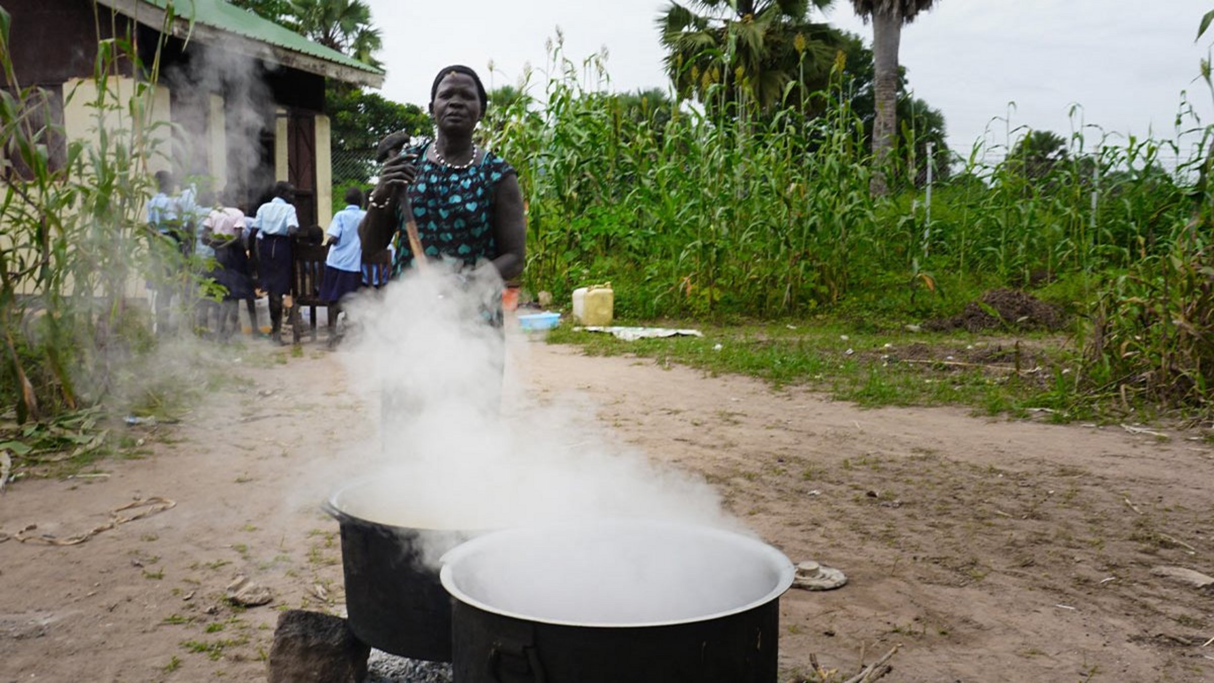 Eine Frau kocht in riesigen Kochtöpfen Mittagessen für Schülerinnen einer südsudanesischen Schule