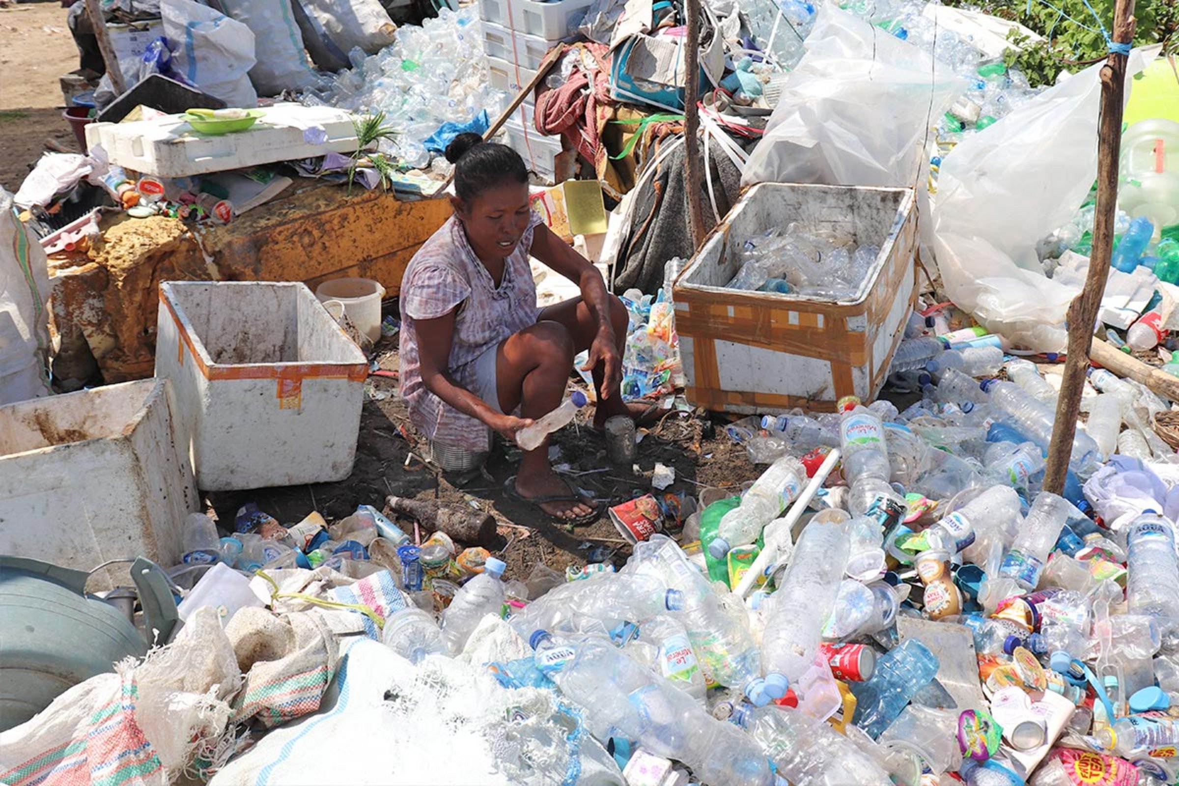 Eine indonesische Frau sitzt zwischen Bergen aus Plastikmüll auf der Suche nach verwertbaren Stoffen