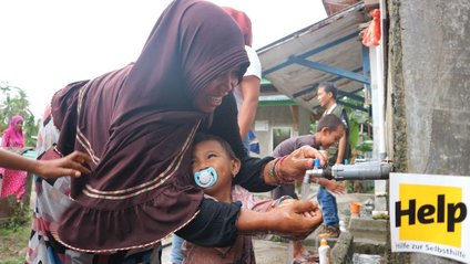 Eine Mutter und ihr Kind waschen sich die Hände an einem Brunnen von Help
