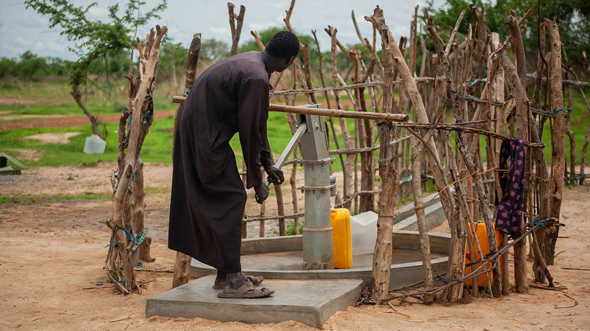 Ein Mann pumpt Wasser aus einem Help-Brunnen