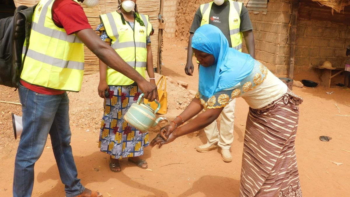 Ein Help-Mitarbeiter erklärt einer Frau in Burkina Faso, wie man sich die Hände wäscht, um sich nicht mit Corona zu infizieren.