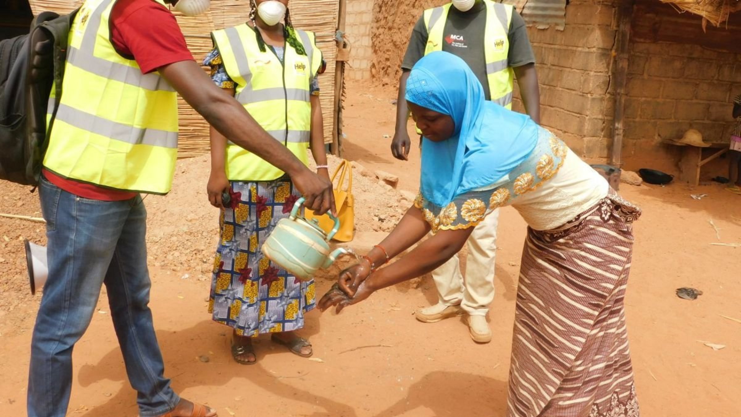 Ein Help-Mitarbeiter erklärt einer Frau in Burkina Faso, wie man sich die Hände wäscht, um sich nicht mit Corona zu infizieren.