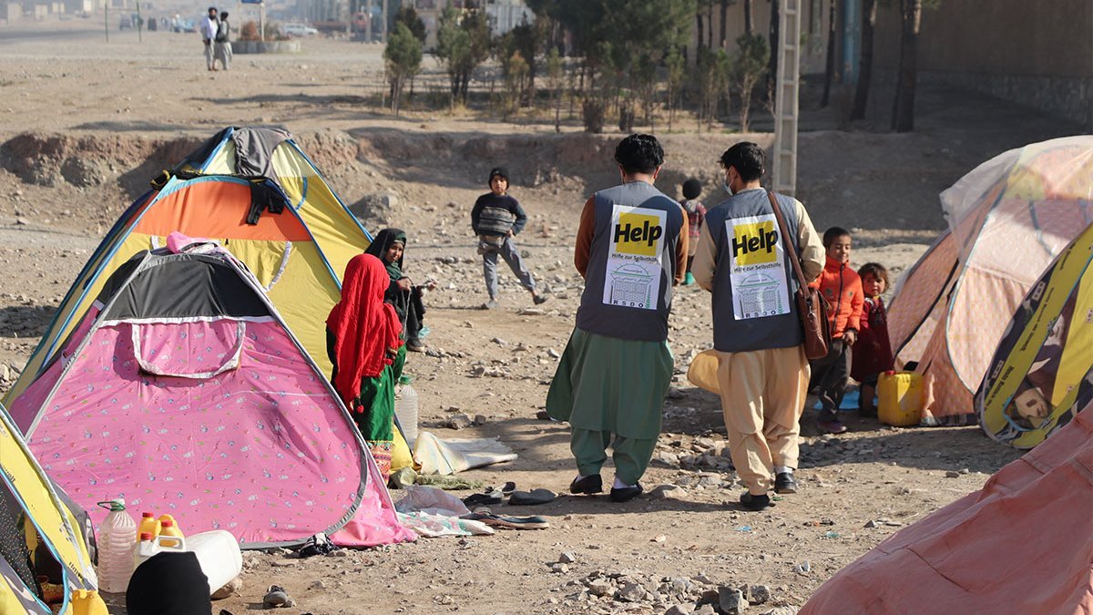 Zwei Help-Mitarbeiter laufen durch ein Flüchtlingslager in Herat, Afghanistan.