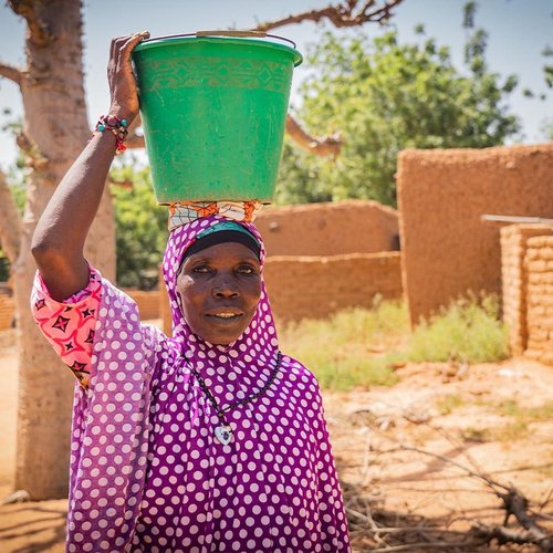 Eine malische Frau trägt einen grünen Eimer Wasser auf dem Kopf