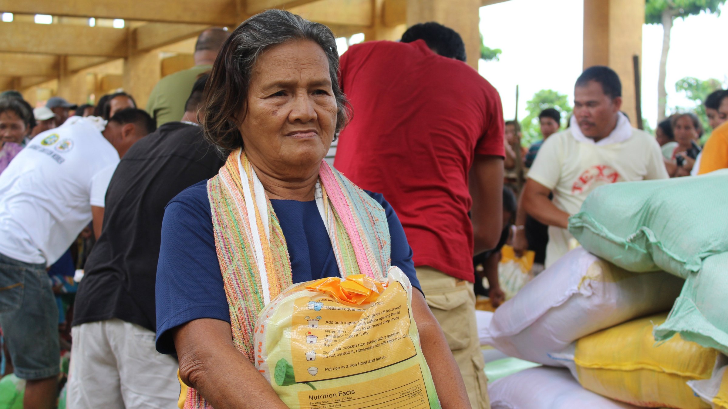 An elderly woman carries a bag of rice