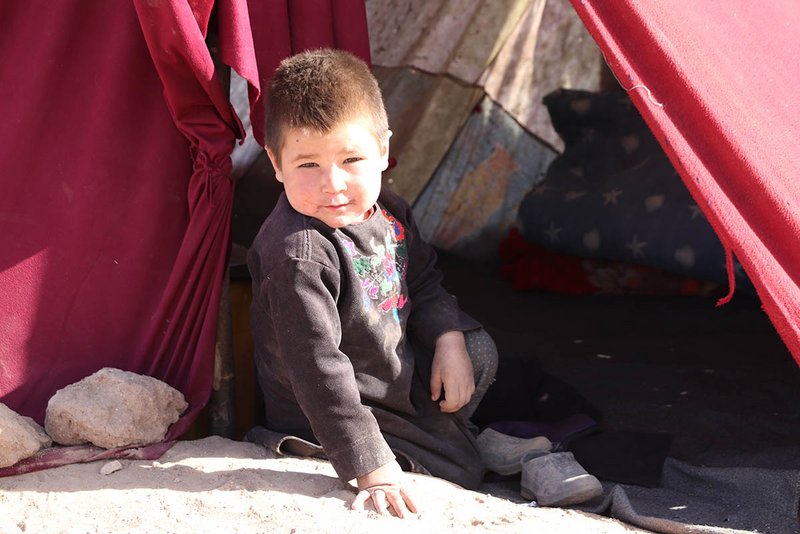 Ein Kind sitzt in einem afghanischen Flüchtlingslager vor einem Zelt