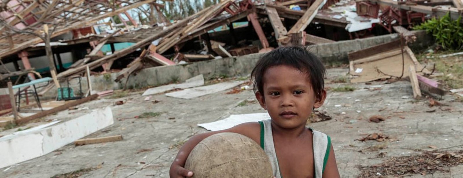 Kleiner Junge mit Ball vor zerstörten Häusern