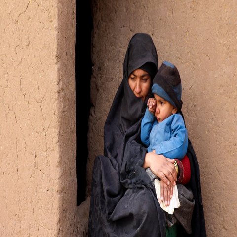Eine afghanische Frau sitzt mit ihrem Kind auf dem Schoß vor einer Wand