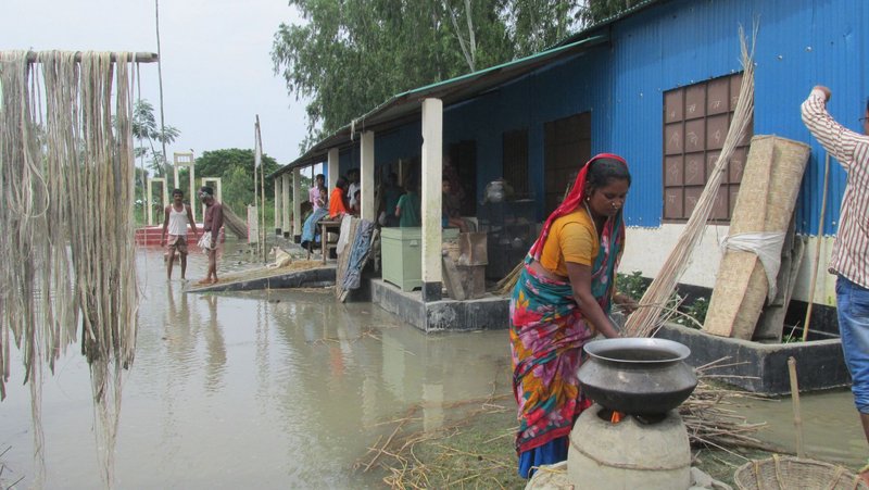 Frau steht in Hochwasser vor Haus in Südasien