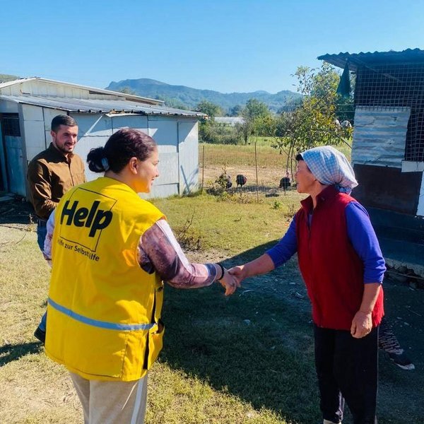 Eine Mitarbeiterin von Help in Albanien begrüßt eine ältere Dame auf dem Land.