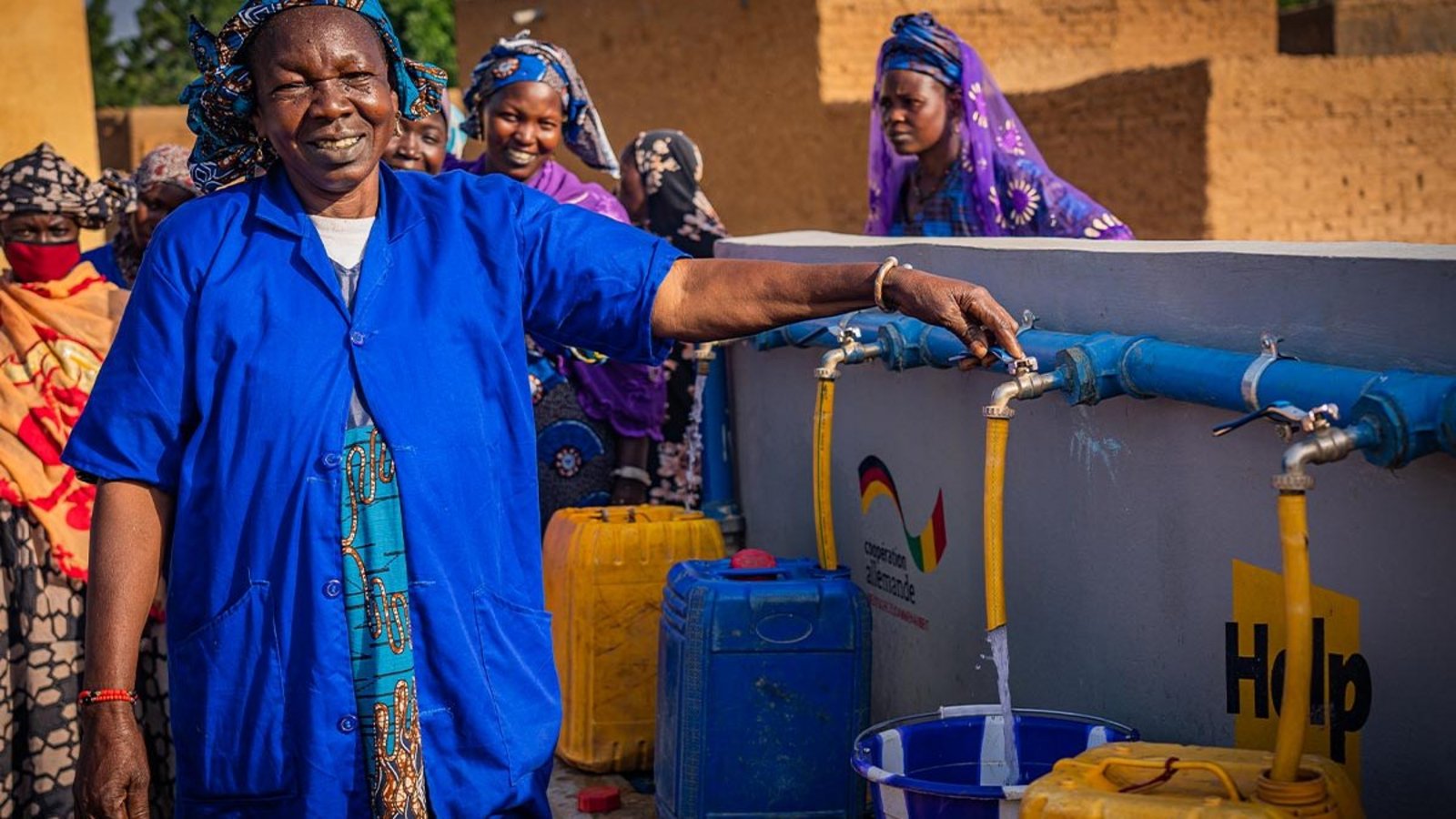 Eine Frau in einem blauen Kleid steht vor einem Help-Brunnen und zapft Wasser ab