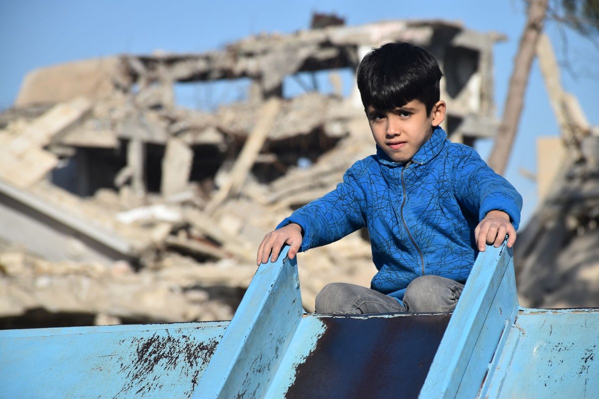 Syrischer Junge vor einem zerstörten Haus auf einer Rutsche