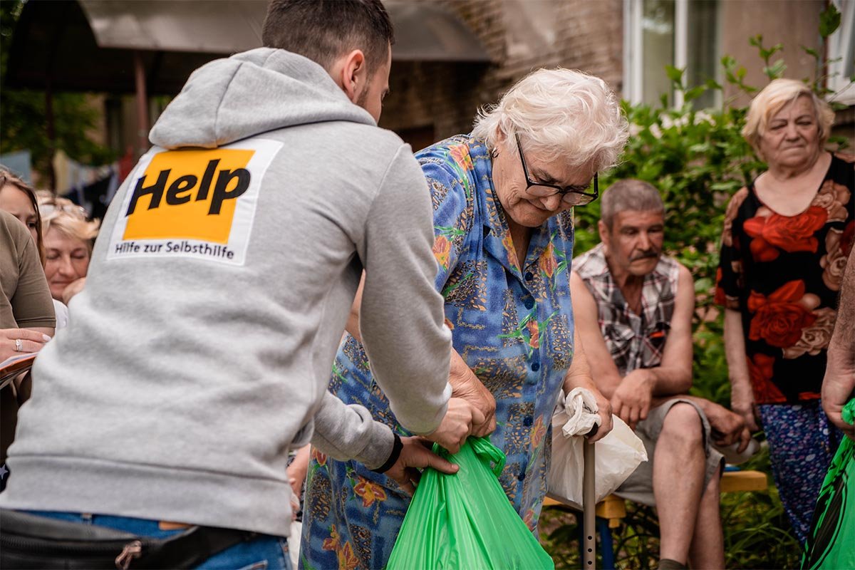 Ein Help-Mitarbeiter überreicht einer älteren Dame Hilfsgüter