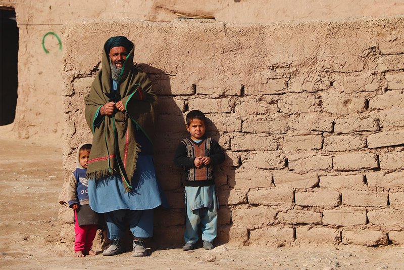 Ein afghanischer Vater und seine zwei Kinder stehen vor einer Mauer.